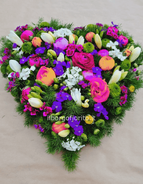 Composizione a forma di cuore con fiori di colori assortiti.
